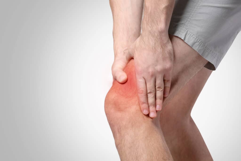 Young man suffering from knee pain on light background. Health care concept