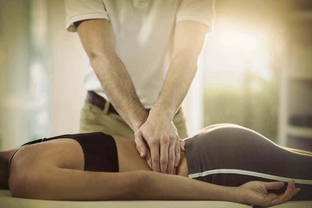 Male physiotherapist giving back massage to female patient in clinic for ongoing pain