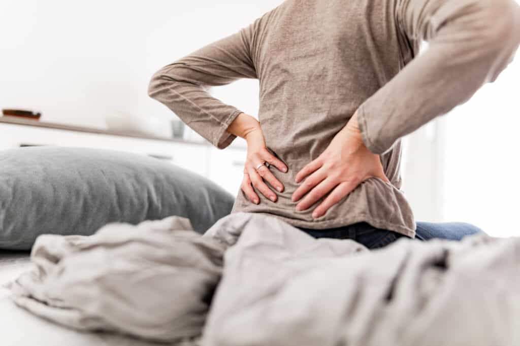 Woman waking up on the bed, morning stretching, pain in the back and hip.