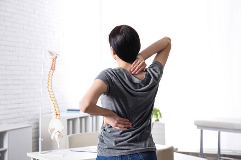 Woman suffering from chronic back pain in back at clinic. Visiting physical therapist