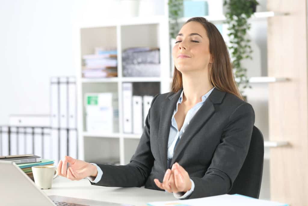 Executive woman stress relieving doing yoga sitting on her desk at the office