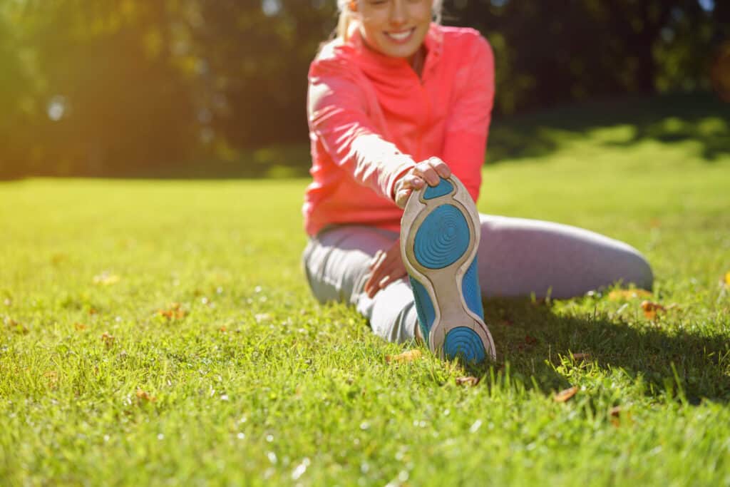 Fit Young Woman Stretching her Leg at the Grassy Park at Early in the Morning. Adopting healthy habits for a brighter future